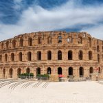 the majestic exterior of the ancient Roman amphitheater El Djem in Tunisia, its grand arches standing proudly under a partly cloudy sky—a must-see on Tailor-Made Tunisia Private Tours.