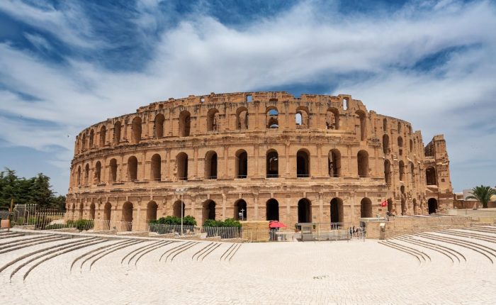 The image captures the majestic exterior of the ancient Roman amphitheater El Djem in Tunisia, its grand arches standing proudly under a partly cloudy sky—a must-see on Tailor-Made Tunisia Private Tours.