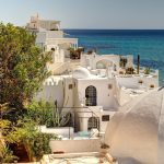White buildings with domed roofs overlook the Mediterranean Sea in a picturesque coastal town, surrounded by greenery and a stone wall. Experience Tunisia's unique charm and explore its beauty with our tailor-made Tunisia private tours.